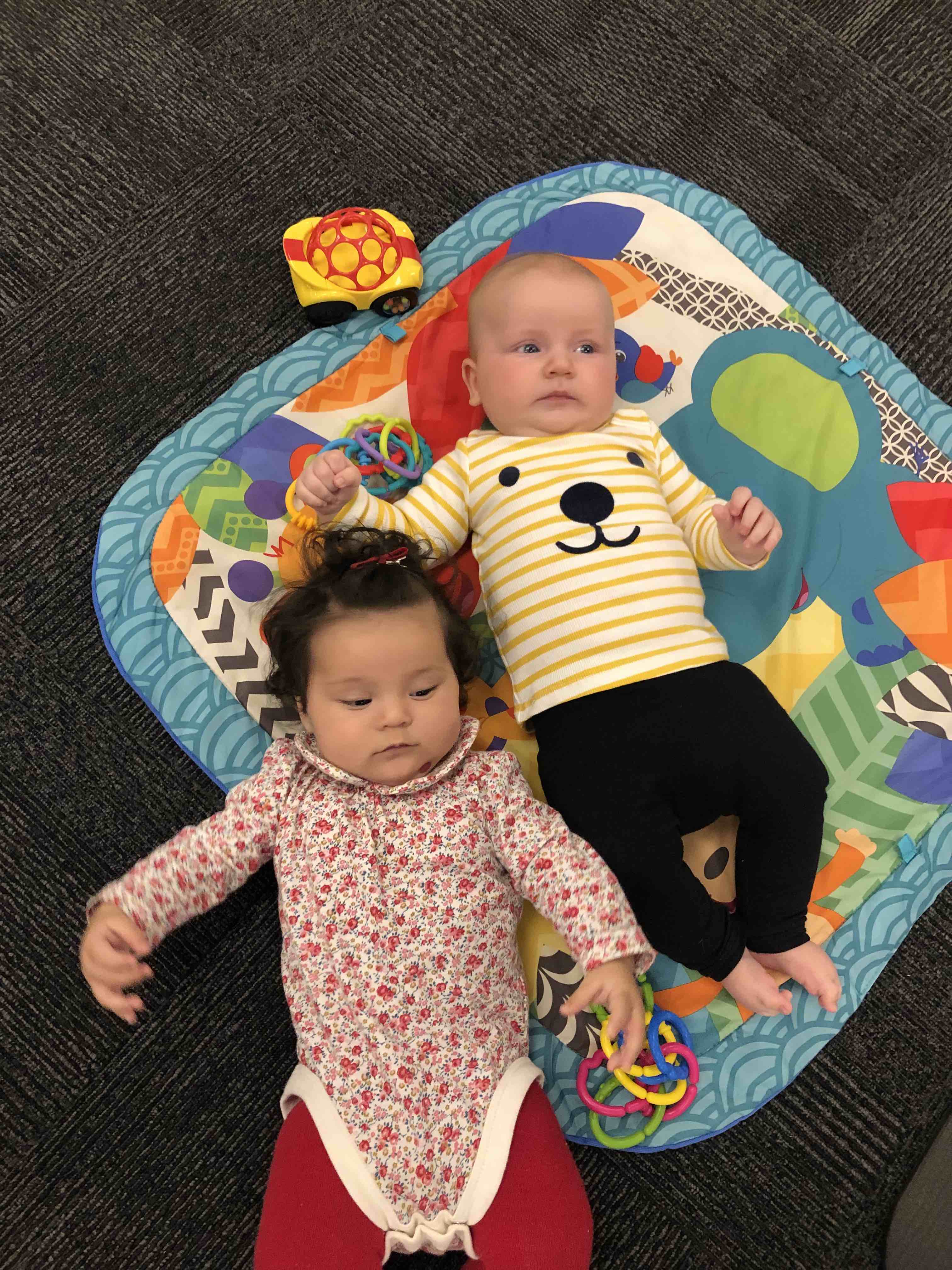 Two babies lying on a rug